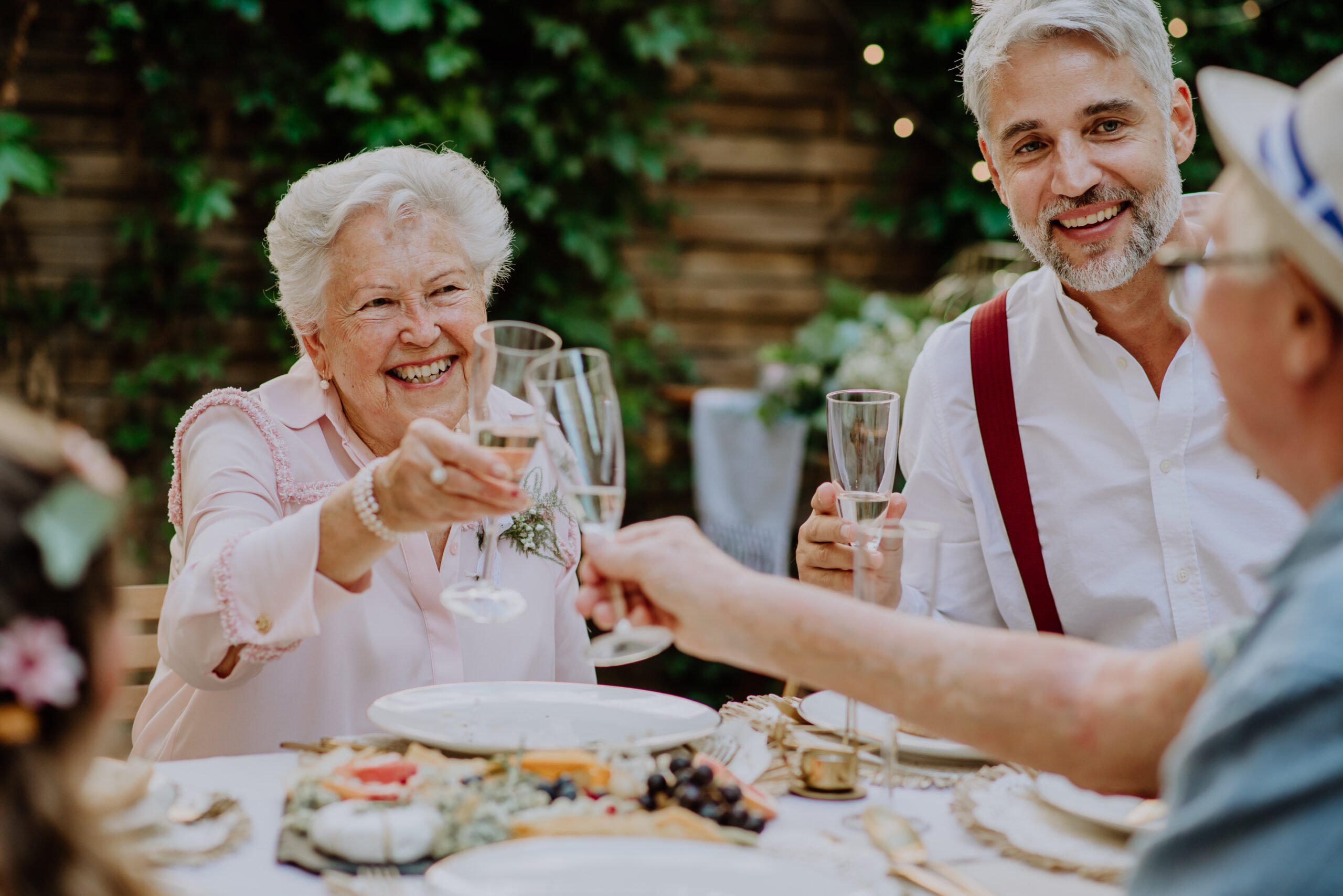 Mature groom toasting with his parents in law at wedding reception outside in backyard.